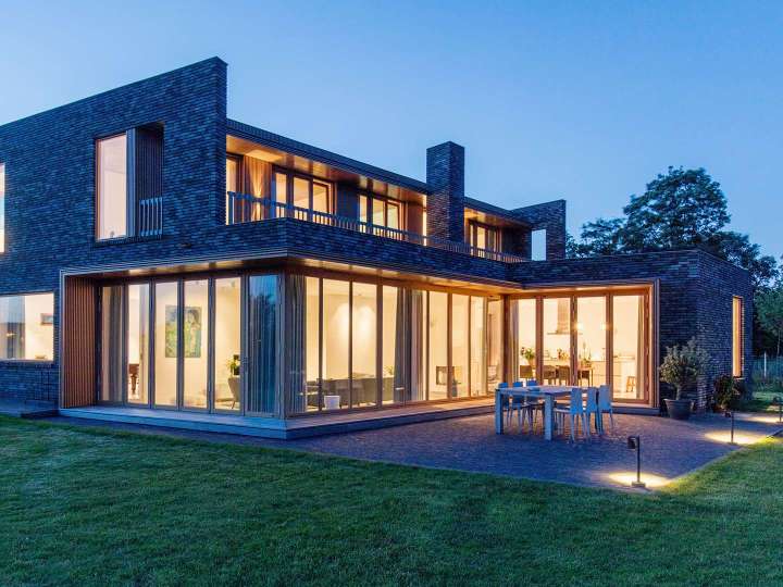 beleuchtetes Haus bei Dämmerung mit vielen bodentiefen Fenstern und Glas-Faltwänden
